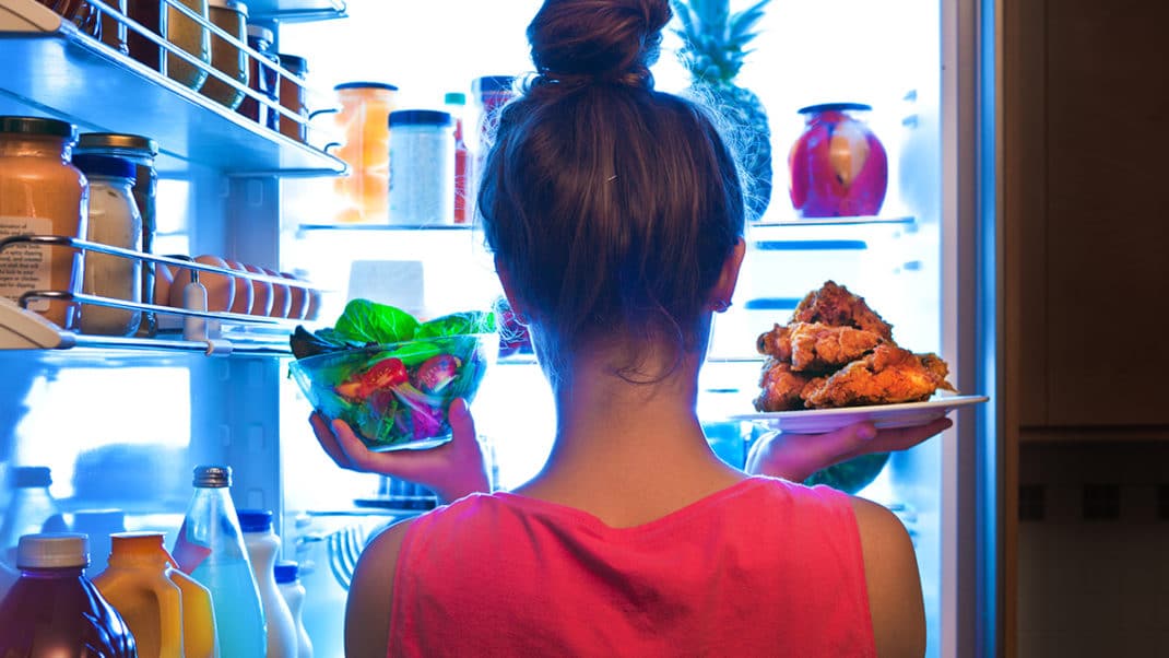 女孩站在冰箱前权衡健康饮食的食物选择